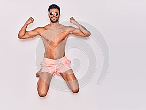 Young handsome hispanic man on vacation wearing swimwear shirtless smiling happy