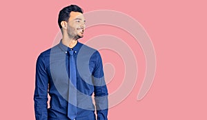 Young handsome hispanic man wearing business clothes looking away to side with smile on face, natural expression