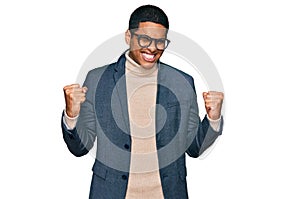 Young handsome hispanic man wearing business jacket and glasses very happy and excited doing winner gesture with arms raised,