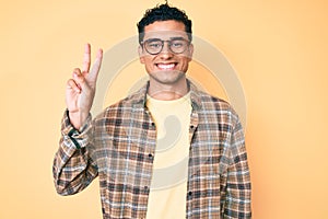 Young handsome hispanic man wearing casual clothes and glasses smiling with happy face winking at the camera doing victory sign