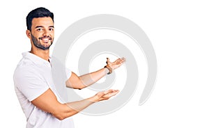 Young handsome hispanic man wearing casual clothes inviting to enter smiling natural with open hand photo