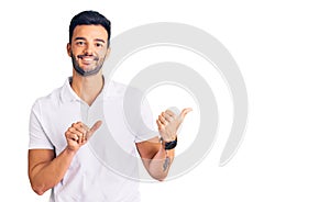 Young handsome hispanic man wearing casual clothes pointing to the back behind with hand and thumbs up, smiling confident