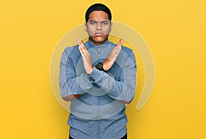 Young handsome hispanic man wearing casual sweatshirt rejection expression crossing arms doing negative sign, angry face