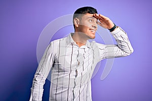 Young handsome hispanic man wearing elegant business shirt standing over purple background very happy and smiling looking far away