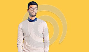 Young handsome hispanic man wearing elegant clothes and glasses smiling looking to the side and staring away thinking