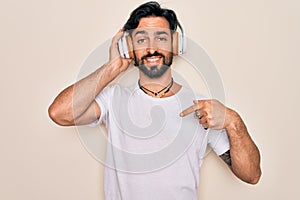Young handsome hispanic man wearing headphones listening to music over isolated background with surprise face pointing finger to