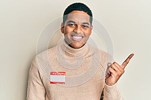 Young handsome hispanic man wearing hello my name is sticker identification smiling happy pointing with hand and finger to the