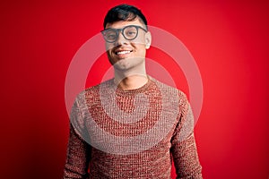 Young handsome hispanic man wearing nerd glasses over red background with a happy and cool smile on face