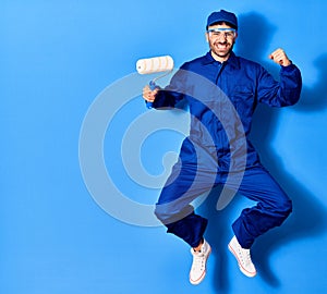 Young handsome hispanic man wearing painter uniform and cap smiling happy