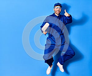 Young handsome hispanic man wearing painter uniform and glasses smiling happy