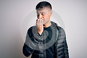 Young handsome hispanic man wearing winter coat standing over white isolated background looking stressed and nervous with hands on
