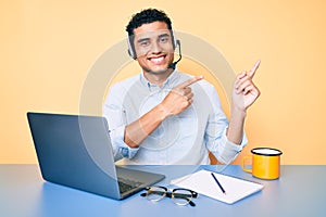 Young handsome hispanic man working at the office wearing operator headset smiling and looking at the camera pointing with two