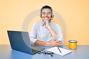 Young handsome hispanic man working at the office wearing operator headset smiling looking confident at the camera with crossed