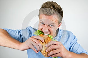 Young handsome hungry man biting fresh sandwich with salad leaf on  white background