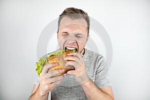 Young handsome hungry man with closed eyes biting fresh sandwich with salad leaf on isolated white background