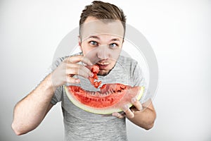 Young handsome hungry man eats fresh watermelon with his hands on isolated white background