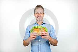 Young handsome hungry man looks hungry and happy holding fresh sandwich with salad on  white background