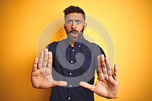 Young handsome indian businessman wearing shirt over isolated yellow background afraid and terrified with fear expression stop