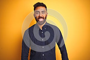 Young handsome indian businessman wearing shirt over isolated yellow background sticking tongue out happy with funny expression