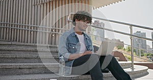 young handsome indian hindu man student freelancer sitting outdoors on steps making video call using laptop computer