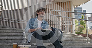 young handsome indian hindu man student freelancer sitting outdoors on steps using laptop computer