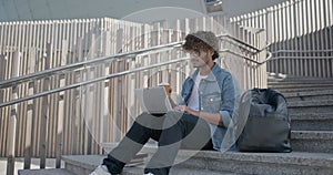 young handsome indian hindu man student freelancer sitting outdoors on steps using laptop computer