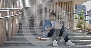 young handsome indian hindu man student freelancer sitting outdoors on steps using laptop computer