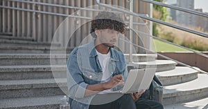 young handsome indian hindu man student freelancer sitting outdoors on steps using laptop computer