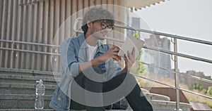 young handsome indian hindu man student freelancer sitting outdoors on steps using tablet pc computer pad