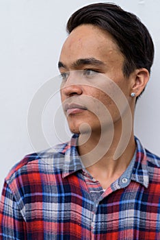 Young handsome Indian man against white wall in the streets outd