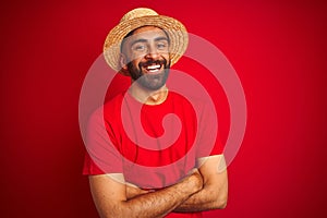 Young handsome indian man wearing t-shirt and hat over isolated red background happy face smiling with crossed arms looking at the