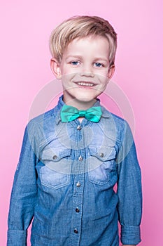 Young handsome kid smiling with blue shirt and butterfly tie. Studio portrait over pink background