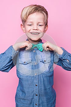 Young handsome kid smiling with blue shirt and butterfly tie. Studio portrait over pink background