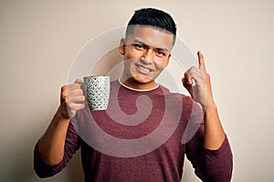 Young handsome latin man drinking cup of coffee over isolated white background surprised with an idea or question pointing finger