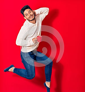 Young handsome latin man smiling happy drinking cup of coffee