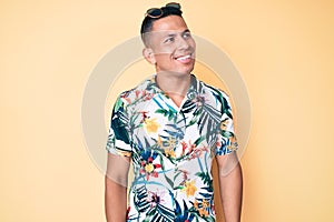 Young handsome latin man wearing summer clothes looking away to side with smile on face, natural expression