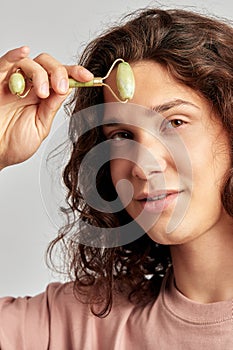 Young handsome long haired guy using jade de-puffing face roller to keep his skin soft and smooth. Caucasian man