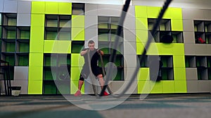 young and handsome male athlete man doing exercises for the muscles of the body with a battle ropes in fitness gym with