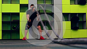 young and handsome male athlete man doing exercises for the muscles of the body with a battle ropes in fitness gym with