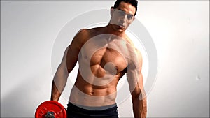 Young handsome male bodybuilder training obliques and abs muscles with dumbbells, against light background