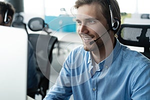 Young handsome male customer support phone operator with headset working in call center