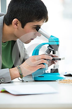 Young handsome male student peering through microscope