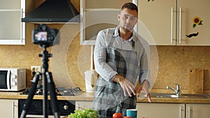 Young handsome man in apron shooting video food blog about cooking on dslr camera in kitchen