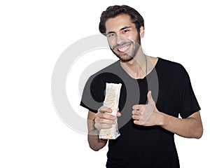 A young handsome man, an Arab, eats with pleasure Donner kebab Shaurma and shows a super sign. Isolation background