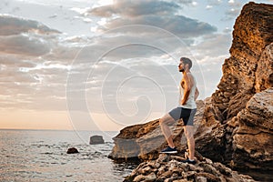 Young handsome man athlete standing at the rocky beach