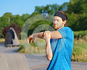 Young handsome man athlete warming up before morning workout in green park