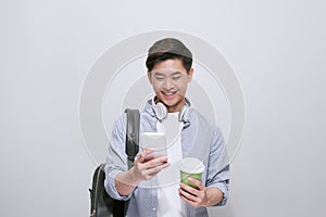 Young handsome man with backpack holding smart phone and coffee. Smiling student going on travel.  on white background