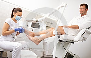 Young handsome man in bathrobe having pedicure treatment