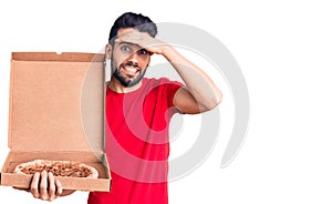 Young handsome man with beard holding delivery cardoboard with italian pizza stressed and frustrated with hand on head, surprised