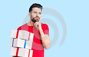 Young handsome man with beard holding gift serious face thinking about question with hand on chin, thoughtful about confusing idea